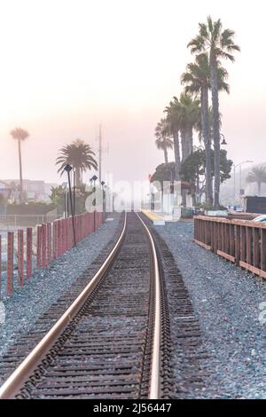 Voies de train avec barrière de poteaux et une vue de l'attente hangar le long des palmiers à San Clemente, CA Banque D'Images