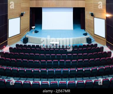 Salle de conférence vide avec chaises rouges et écran vide Banque D'Images