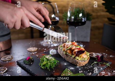 la personne mange un sandwich frais avec de l'avocat, du poisson frit au saumon rouge, des algues et du vin Banque D'Images