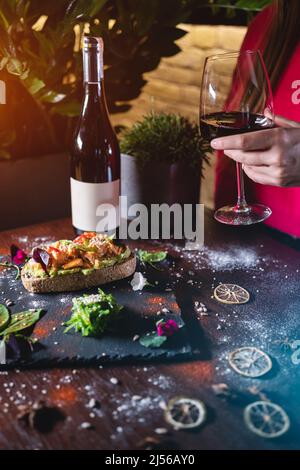 la personne mange un sandwich frais avec de l'avocat, du poisson frit au saumon rouge, des algues et du vin Banque D'Images