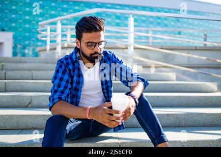 l'homme d'arabie chélat avec une tasse de cacao est assis sur les escaliers à l'extérieur Banque D'Images