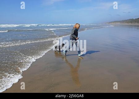 Une femme d'âge moyen joue avec son épagneul cocker américain sur une plage près de Yachats, Oregon, sur la côte Pacifique. Banque D'Images