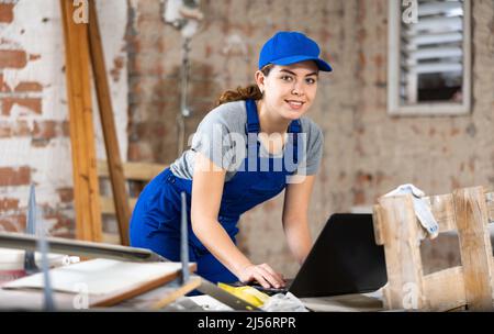 Femme de créateur souriante avec ordinateur portable examinant le chantier de construction Banque D'Images