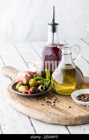 Vinaigre d'huile et de vin rouge sur une planche de bois avec olives et grains de poivre. Banque D'Images