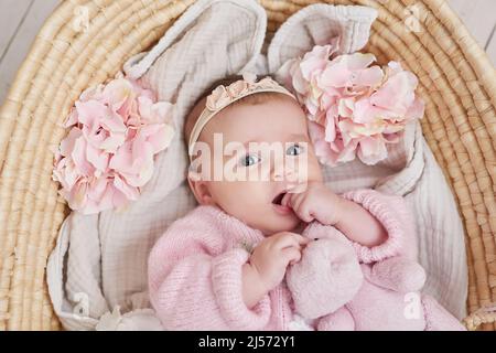 Adorable petite fille en vêtements tricotés et couronne avec jouet ours en peluche. Arrière-plan de printemps avec des fleurs. Journée de la protection des enfants. Carte de vœux de fête des mères. Banque D'Images