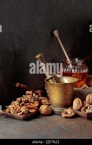 Noix, vieux mortier de laiton et miel sur une table de cuisine. Banque D'Images