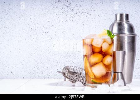 Cocktail au rhum, au citron vert et au cola Cuba libre. Boisson froide de Coca-Cola d'été avec jus d'agrumes, glaçons et feuilles de menthe, carrelage blanc soleil fond éclairé c Banque D'Images