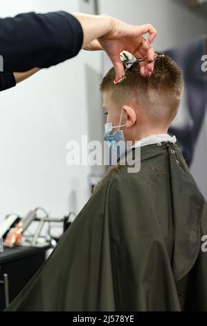 Coupe de cheveux pour enfants dans la barbershop, coupe de cheveux élégante et moderne pour les écoliers, travail pendant la pandémie, coupe de cheveux pour enfants avec des ciseaux. Banque D'Images