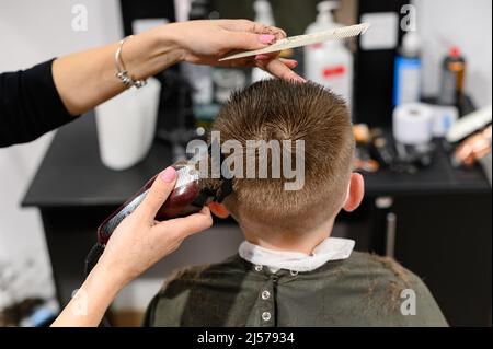 Coupe de cheveux pour enfants dans la barbershop, coupe de cheveux élégante et moderne pour les écoliers, travail pendant la pandémie, coupe de cheveux pour enfants avec des ciseaux. Banque D'Images