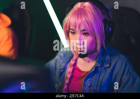 Belle concentrée asiatique femme joueur dans le casque et perruque rose jouant des jeux vidéo copier espace concept moyen gros plan. Photo de haute qualité Banque D'Images
