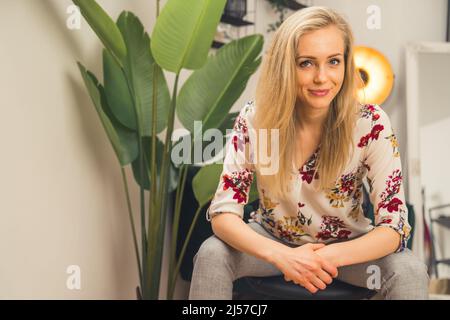 La femme européenne blonde sûre d'elle-même est assise les mains pliantes, plante en pot à côté de l'espace de copie . Photo de haute qualité Banque D'Images