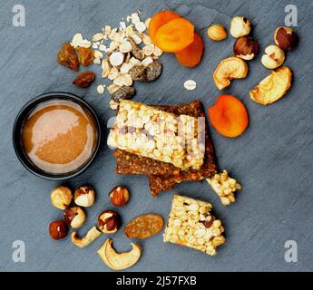 Agencement de barres granola utiles avec muesli, noix, abricots séchés et bol de miel en gros plan sur fond de pierre noire. Vue de dessus Banque D'Images