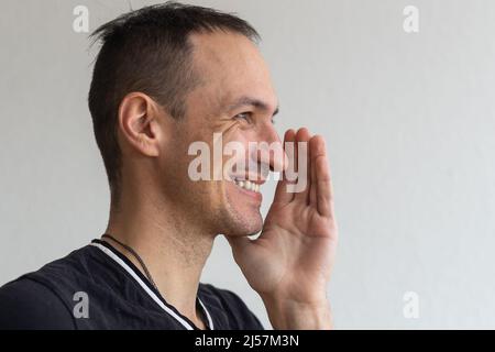 Homme souriant positif avec barbe tenant le doigt près des lèvres montrant le geste shh, gardant les secrets préparer la surprise. Prise de vue en studio isolée sur blanc Banque D'Images