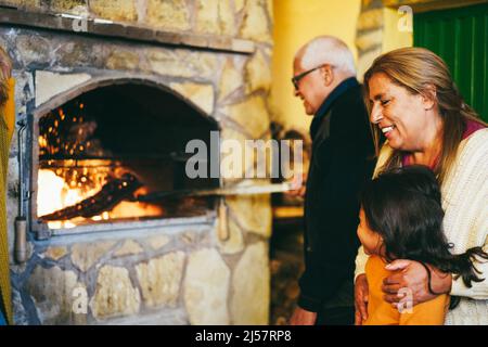 Les grands-parents heureux cuisinant ensemble sur un foyer à bois avec une petite-fille sur le patio de la maison - Focus sur le visage de fille Banque D'Images