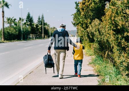 Vue arrière de père et de fils marchant près de la route de la ville. Papa tenant le dos de son enfant lors d'une promenade dans la ville du sud. Homme et garçon allant à l'école Banque D'Images