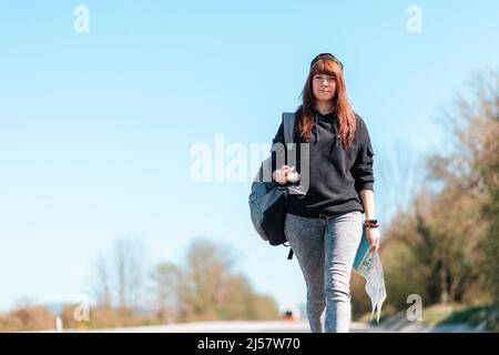 Une jeune femme souriante marche le long de la route avec une carte entre ses mains. Extérieur. Copier l'espace. Concept de randonnée et de voyage local. Banque D'Images
