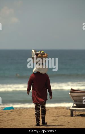 Une femme marchant alors qu'elle vend des fruits frais sur la plage de Kuta à Kuta, Badung, Bali, Indonésie. Banque D'Images