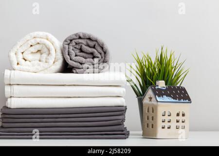 Une pile de draps gris et blancs, de draps et de serviettes en tissu éponge sur la table. Une plante en pot et une petite maison de jouet Banque D'Images