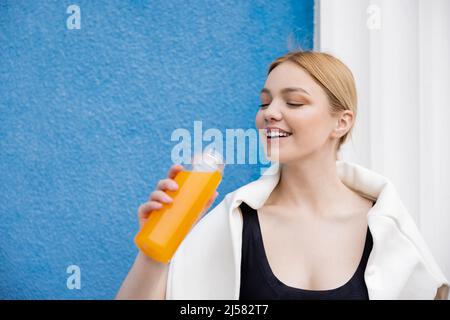 ravie sportswoman tenant une bouteille de jus d'orange rafraîchissant près du mur bleu Banque D'Images