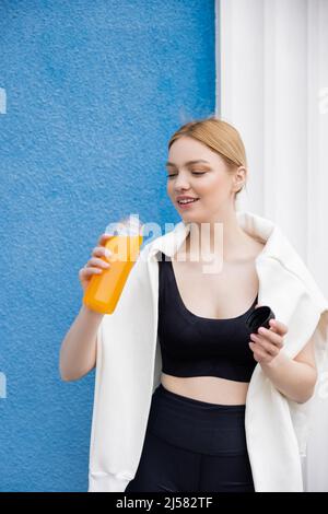 jeune femme sportive tenant une bouteille avec du jus d'orange frais près du mur bleu Banque D'Images