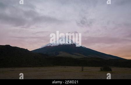 Vue panoramique sur le volcan Cotopaxi derrière un champ vert sans personnes dans un lever de soleil nuageux - Equateur Banque D'Images