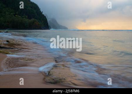 Les vagues se délavent sur la plage de Ke'e, dans le parc national de Ha'ena, à Kauai, à Hawaï. Les nuages de tempête obscurcissent la côte de Na Pali au loin. Banque D'Images