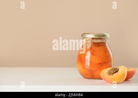 Confiture d'abricot maison dans un pot en verre sur fond beige. Récolte d'été et conserves Banque D'Images