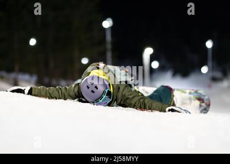 Fille de snowboardeur couchée face vers le bas sur la pente. Ski de nuit dans la station d'hiver. Banque D'Images