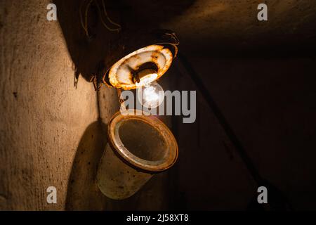 Une vieille ampoule à incandescence dans un ancien plafonnier rouillé dans un sous-sol sombre gros plan Banque D'Images