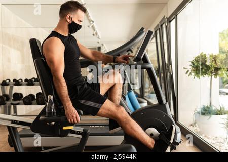 Jeune homme sportif portant un masque de prévention pendant son entraînement en salle de gym Banque D'Images