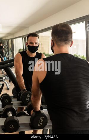 Nouveau concept normal.Jeune homme sportif portant un masque de prévention pendant son entraînement en salle de gym. Banque D'Images