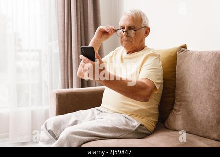 Un homme âgé portant des lunettes utilise un smartphone à la maison Banque D'Images