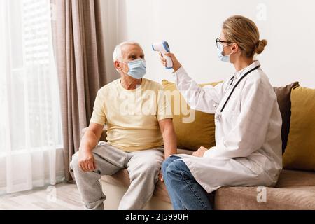 Jeune femme médecin vérifiant la température du corps à l'homme âgé pendant la visite à domicile Banque D'Images