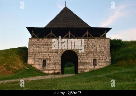 Une grande tour d'une forteresse médiévale en pierre avec une entrée voûtée, des échappatoires et des remparts de terre sur les côtés Banque D'Images