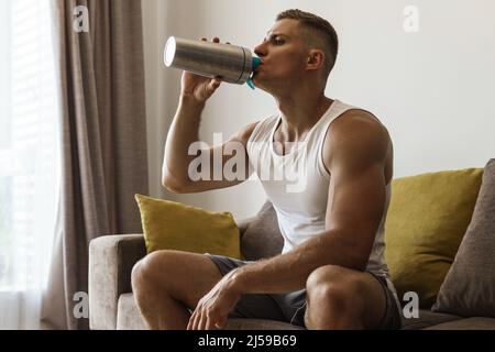 Jeune et musclé homme boire des protéines secouer après l'entraînement intense à la maison Banque D'Images