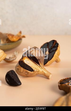 Composition conceptuelle de gousses d'ail noires fermentées. Bulbes et gousses d'ail noir sur une table beige. Nutrition saine, nourriture végétarienne Banque D'Images