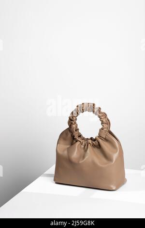 Sac à main couleur café en cuir artificiel sur fond blanc minimaliste. Un sac en similicuir posé sur une table blanche Banque D'Images