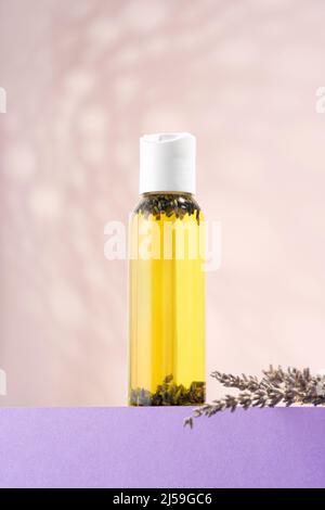 Une bouteille d'huile essentielle de lavande, fleurs de lavande sur un podium violet. Huile essentielle cosmétique pour bains du corps sur fond clair. Phytothérapie Banque D'Images