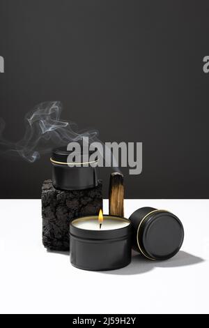 Composition de Palo santo en feu et de bougies en cire de soja dans des pots noirs en métal élégants sur une table blanche sur fond sombre. ECO Banque D'Images