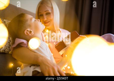 Joyeux Noël, mère de famille et enfants avec cadeau magique à la maison quarantaine auto-isolement virus covid guirlande lueur Banque D'Images