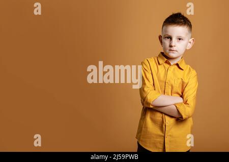 Photo d'un beau garçon d'école attrayant et gai debout avec ses bras croisés devant l'appareil photo tout en étant isolé sur fond jaune. Photo de haute qualité Banque D'Images