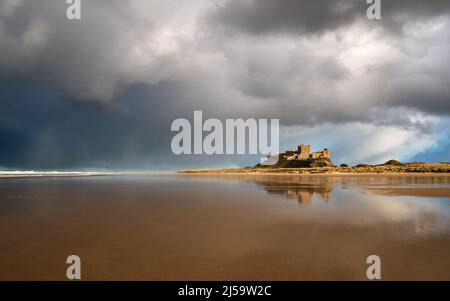 Le château de Bamburgh brille tandis que le soleil se fait jour et que le coucher du soleil est spectaculaire et traverse la côte de Northumberland lors d'une soirée de printemps changeante. Banque D'Images