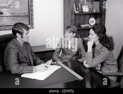 1970S MÈRE ET FILS ADOLESCENT AYANT UNE CONVERSATION AVEC L'ORIENTATION PRINCIPALE DE L'ÉCOLE CONSEILLER AGENT DE BANQUE AVOCAT OU THÉRAPEUTE - J13000 HAR001 HARS ÉDUCATION MOM À L'INTÉRIEUR AVOCAT NOSTALGIQUE PAIRE D'HOMMES D'AFFAIRES SUBURBAIN MÈRES VIEUX TEMPS NOSTALGIE CONSULTATION VIEILLE MODE CONVERSATION 1 JUVÉNILE COMMUNICATION CARRIÈRE FILS MODE DE VIE CONSEILLER FEMMES ESPACE DE COPIE DEMI-LONGUEUR FEMMES PERSONNES S'OCCUPANT HOMMES AGENT ADOLESCENT GARÇON PROFESSION B&W OBJECTIFS SANTÉ ÉCOLES CONSEILS SUIT ET LIE PROFESSION FOURNISSEUR DE L'ANGLE ÉLEVÉ PRATICIENS GUÉRISON ET CARRIÈRES CHOIX MÉDECINS AUTORITÉ EN SOINS DE SANTÉ Banque D'Images