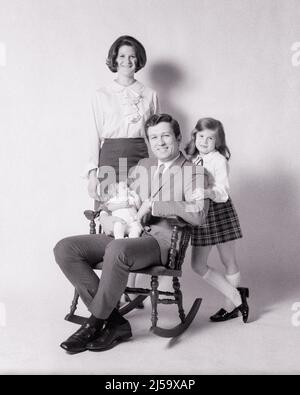 1970S PORTRAIT DE FAMILLE PÈRE ASSIS DANS LE ROCKER TENANT BÉBÉ MÈRE ET FILLE DEBOUT À CÔTÉ DE LUI SOURIANT REGARDANT L'APPAREIL PHOTO - J13224 HAR001 HARS FUN LADY COUPLES MARI DAD BÉBÉS QUATRE MOM VÊTEMENTS À L'INTÉRIEUR NOSTALGIQUE PAIRE 4 BEAUTÉ SUBURBAIN URBAIN MÈRES VIEUX TEMPS FUTUR NOSTALGIE VIEILLE MODE SŒUR 1 STYLE JUVÉNILE COMMUNICATION JEUNE ADULTE ÉQUILIBRE TRAVAIL D'ÉQUIPE BÉBÉ FILS FORTS FAMILLES HEUREUSES JOIE STYLE DE VIE SATISFACTION CÉLÉBRATION FEMMES MARIÉ STUDIO SHOT ROCKER CONJOINT ÉPOUX COPIER ESPACE PLEINE LONGUEUR DEMI-LONGUEUR FEMMES FILLES PERSONNES S'OCCUPANT HOMMES FRÈRES ET SŒURS CONFIANCE SŒURS PÈRES B&W. Banque D'Images