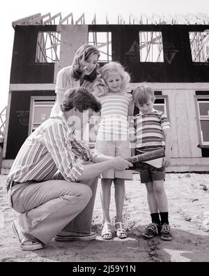 1970S MÈRE PÈRE ET DEUX ENFANTS DEBOUT DEVANT LA MAISON SOUS CONSTRUCTION PÈRE AGENOUILLÉ TENANT DES PLANS DE LA MAISON - J14171 HAR001 HARS 4 SUBURBAIN MÈRES VIEUX TEMPS NOSTALGIE FRÈRE VIEILLE MODE SOEUR JUVÉNILE STYLE DESIGN FILS FAMILLES STYLE DE VIE ARCHITECTURE FEMMES MAISONS FRÈRES MARIÉS SITE CONJOINT ÉPOUX MAISON VIE COPIE ESPACE PLEINE LONGUEUR DEMI-LONGUEUR FEMMES FILLES PERSONNES RÉSIDENTIEL HOMMES BÂTIMENTS FRÈRES SŒURS SŒURS BLUEPRINTS PÈRES B&W PARTENAIRE AGENOUILLER STRUCTURE NOUVELLE MAISON ET DADS EXTÉRIEUR BAS ANGLE MAISONS FRÈRE RÉSIDENCE ADULTE MOYEN-ADULTE HOMME MOYEN-ADULTE FEMME MAMAN ÉPOUSES Banque D'Images