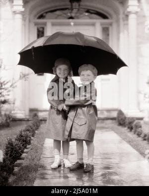 1930S GARÇON ET FILLE FRÈRE SOEUR PORTANT DES MANTEAUX DE PLUIE REGARDANT LA CAMÉRA DEBOUT SOUS LE GRAND PARAPLUIE PARTAGÉ AVANT LA MAISON DE BANLIEUE - J6290 HAR001 HARS VIEILLE MODE SOEUR 1 JUVÉNILE HUMIDE ACCUEIL AMI HEUREUX JOIE VIE SATISFACTION FEMMES MAISONS FRÈRES MANTEAUX SANTÉ MAISON VIE COPIE ESPACE AMITIÉ PLEINE LONGUEUR PLUVIEUX PERSONNES RÉSIDENTIELLES SOINS MÂLES PLUIE BÂTIMENTS FRÈRES ET SŒURS B&W CONTACT VISUEL AVANT BONHEUR GAI ET FIERTÉ PARTAGÉ MAISONS FRÈRE SOURIRES PLUVIEUX JOUR CONNEXION AMICALE JOYEUSE RÉSIDENCE ÉLÉGANTE EN FACE DE LA CROISSANCE DE LA COOPÉRATION LA TOGETHETÉ DES JUVÉNILES AU PRINTEMPS Banque D'Images