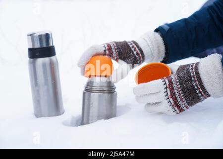 Les mains en gants tiennent un thermos sur la neige. Thé dans un thermos en hiver sur la neige Banque D'Images