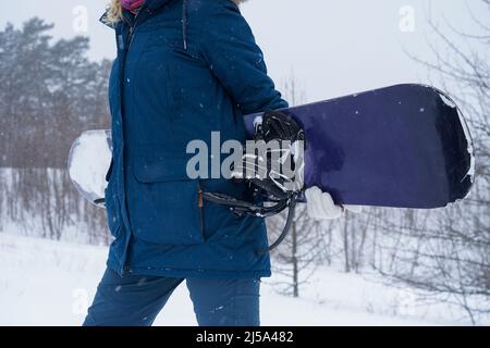 La fille tient un snowboard dans ses mains, elle est vêtue d'une veste de montagne et d'un casque Banque D'Images