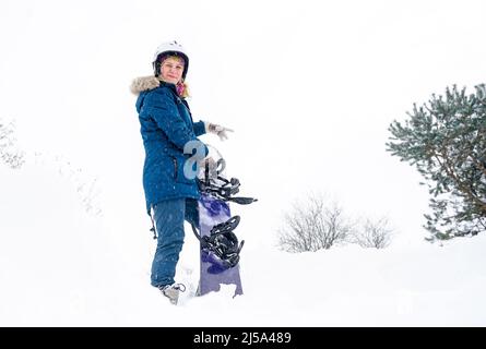 La fille tient un snowboard dans ses mains, elle est vêtue d'une veste de montagne et d'un casque Banque D'Images