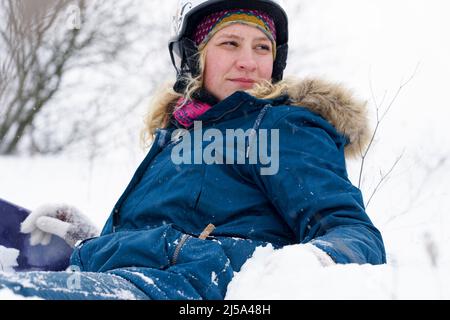 Portrait d'une jeune snowboardeuse dans la neige. Une fille dans un casque de ski et une veste repose sur la neige. Banque D'Images